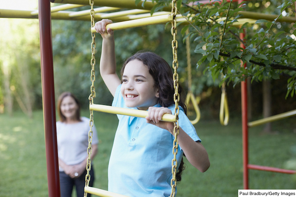 Young girl outdoors at playground climbing with senior woman in background smiling