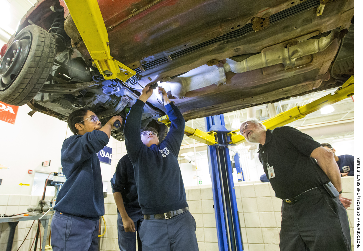 Worcester Technical High School teacher Louis Desy, right, watches as Zaire Peart, left, holds a flashlight for Kyle Dipilato, who is disassembling a car donated by a local salvage company.