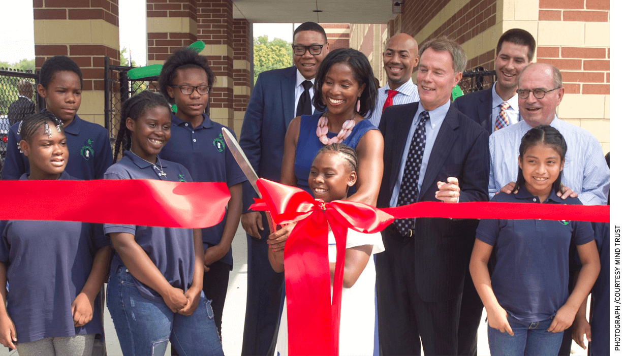 Mariama Shaheed Carson (in blue dress), then Superintendent Lewis Ferebee, Indianapolis Mayor Joe Hogsett, and Brandon Brown cut a ribbon with students in July 2016 to celebrate the opening of Global Prep Academy. The school offers “two-way immersion” in English and Spanish.