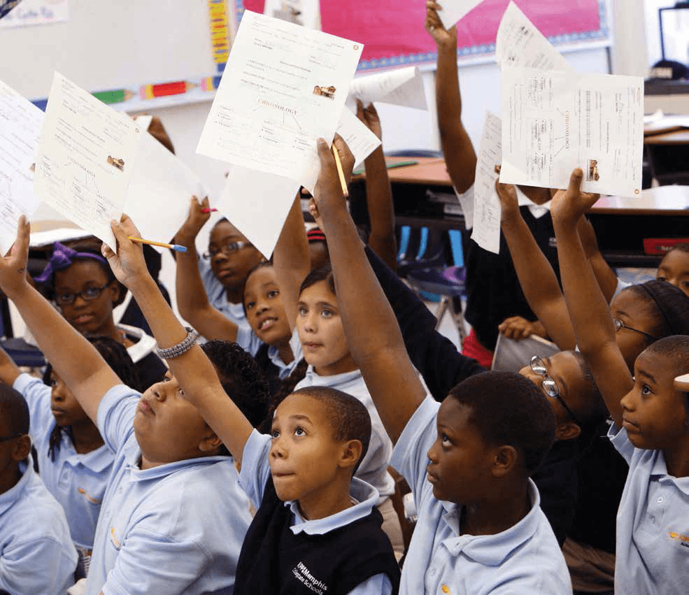 Students raising sheets of paper in the air in a classroom