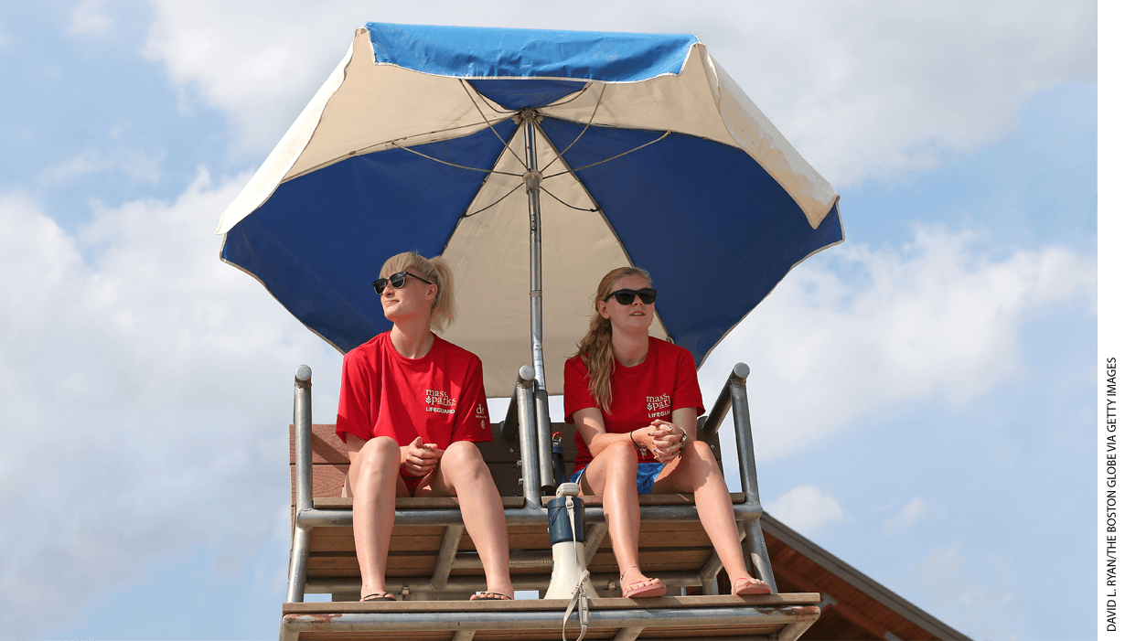 Two lifeguards sitting in a chair under an umbrella