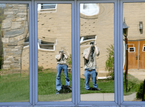 Man taking a photo and facing a funhouse mirror.