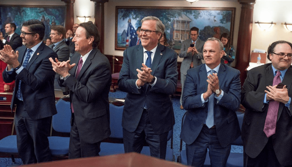 Former Florida Gov. Jeb Bush, center, applauds on the floor of the Florida House of Representatives after the passage of the Family Empowerment Scholarship program.