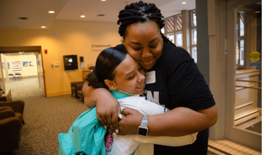 Crystalle Green, the Communities in Schools of Mid-America site coordinator for Cross- roads Preparatory Academy in Kansas City, Missouri, hugs a student headed to class during a "Motivational Monday" event.