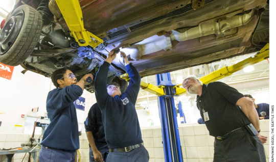 Worcester Technical High School teacher Louis Desy, right, watches as Zaire Peart, left, holds a flashlight for Kyle Dipilato, who is disassembling a car donated by a local salvage company.