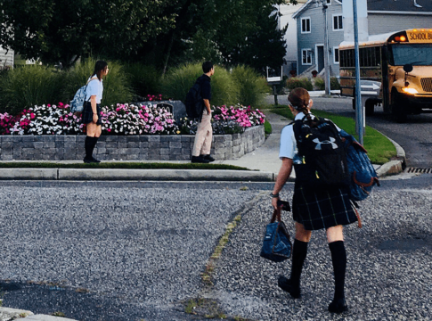 Students wearing school uniforms wait for a bus.