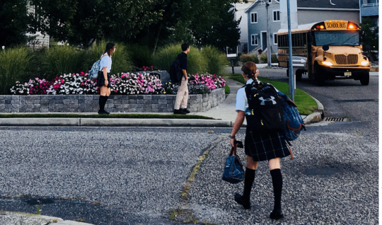 Students wearing school uniforms wait for a bus.