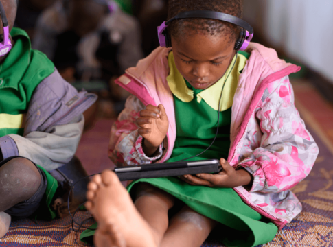 Girl wearing headphones sits and reads on a tablet computer