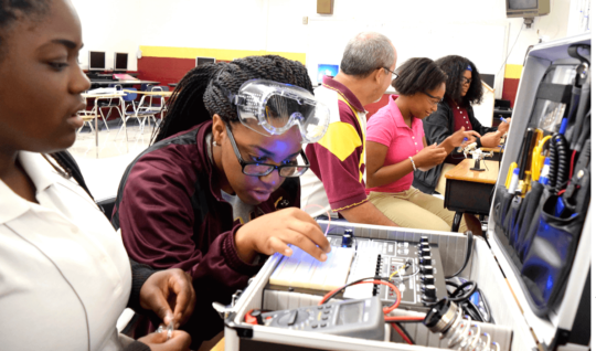 Training for high-tech: In Chattanooga, Tennessee, Tyner Academy students (from left) Jada Beckett and Takayla Sanford work on building circuits, while “mechatronics” teacher Bryan Robinson instructs Brookeana Willams and Noemy Marberry about soldering.