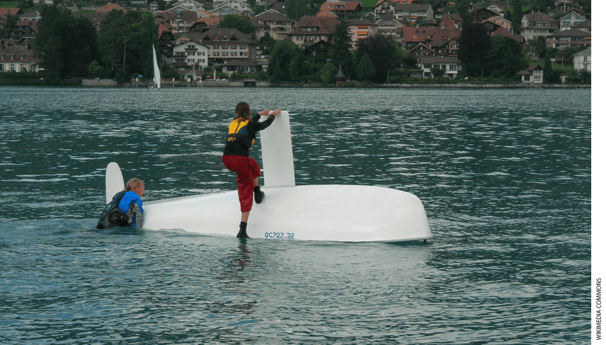 Two sailors on a turtled sailboat