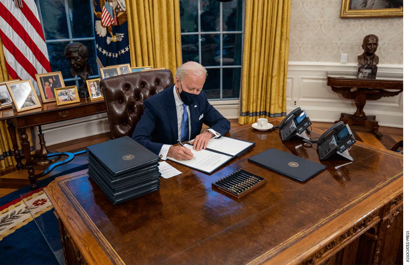 United States President Joe Biden signs executive order on Covid-19 during his first minutes in the Oval Office, Wednesday, Jan. 20, 2021.