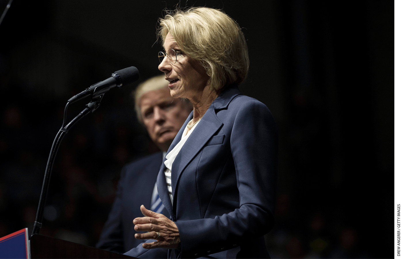 President-elect Donald Trump looks on as Betsy DeVos, his nominee for Secretary of Education, speaks at the DeltaPlex Arena, December 9, 2016 in Grand Rapids, Michigan.