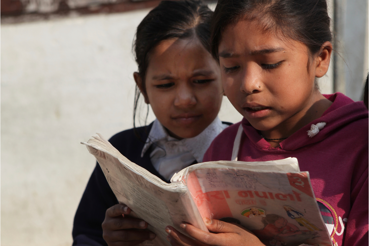 Two young schoolgirls read a Nepali textbook during recess outside their classroom in Kathmandu, Nepal.