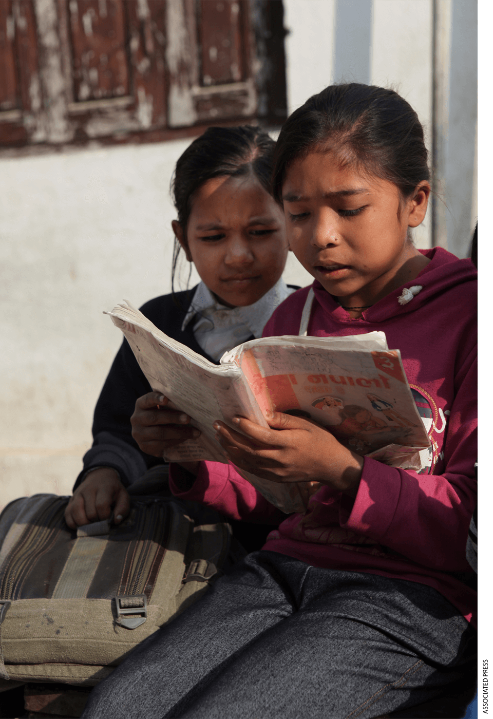 Two young schoolgirls read a Nepali textbook during recess outside their classroom in Kathmandu, Nepal.
