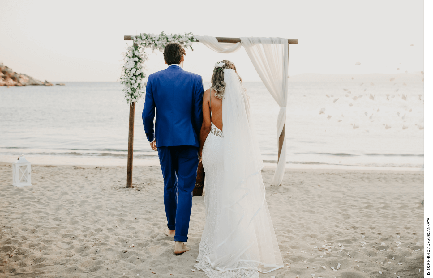 A bride and groom walk on a beach