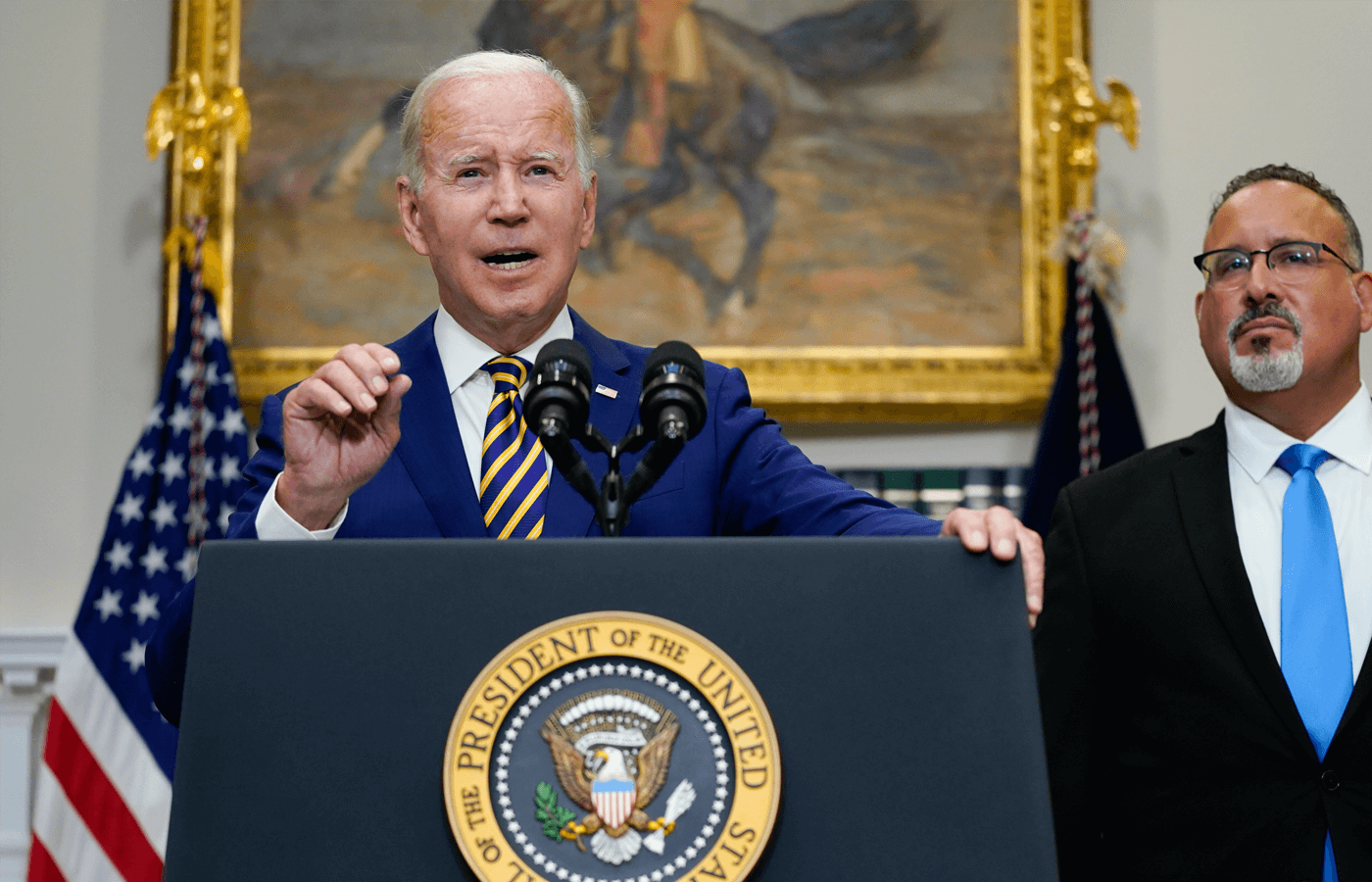 President Joe Biden speaks about student loan debt forgiveness in the Roosevelt Room of the White House, Wednesday, Aug. 24, 2022, in Washington. Education Secretary Miguel Cardona listens at right.