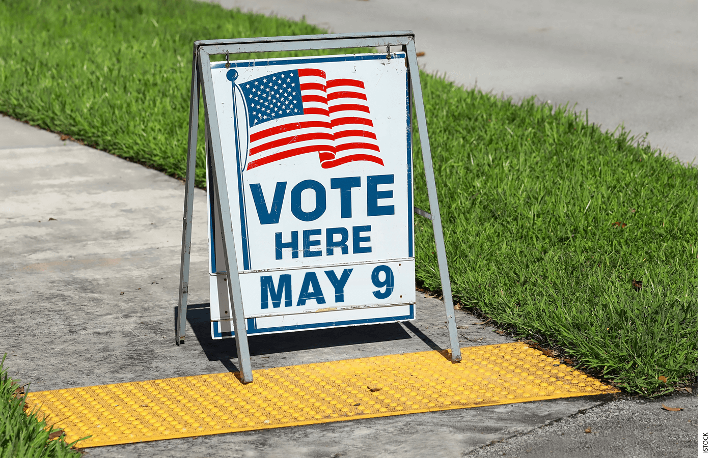 A sandwich board that reads "VOTE HERE MAY 9"