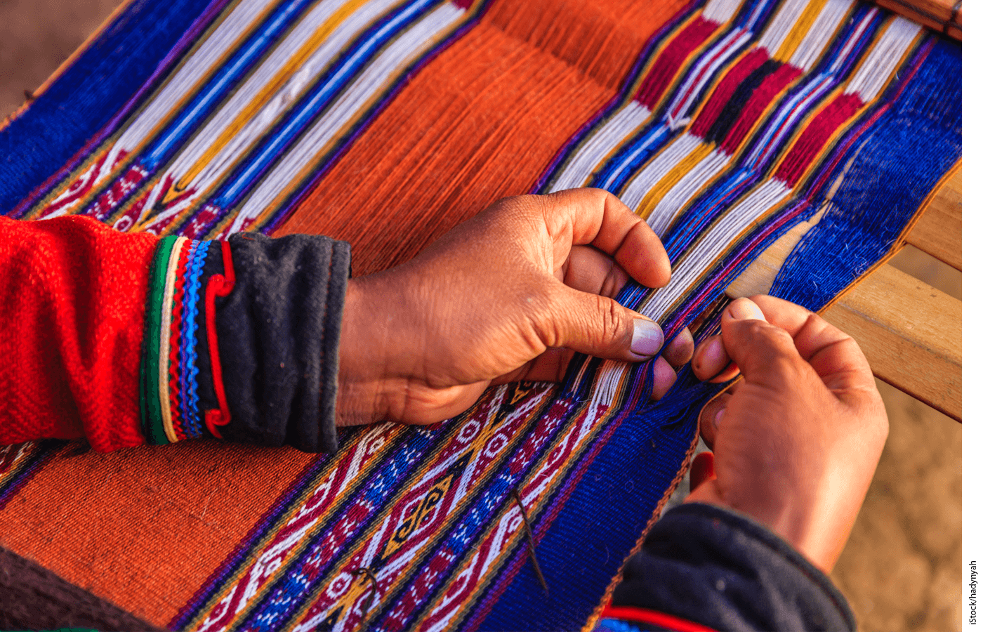 A closeup of two hands weaving fabric on a loom