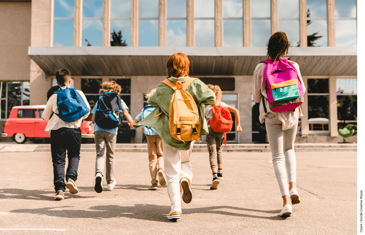 Students wearing backpacks walking towards a school