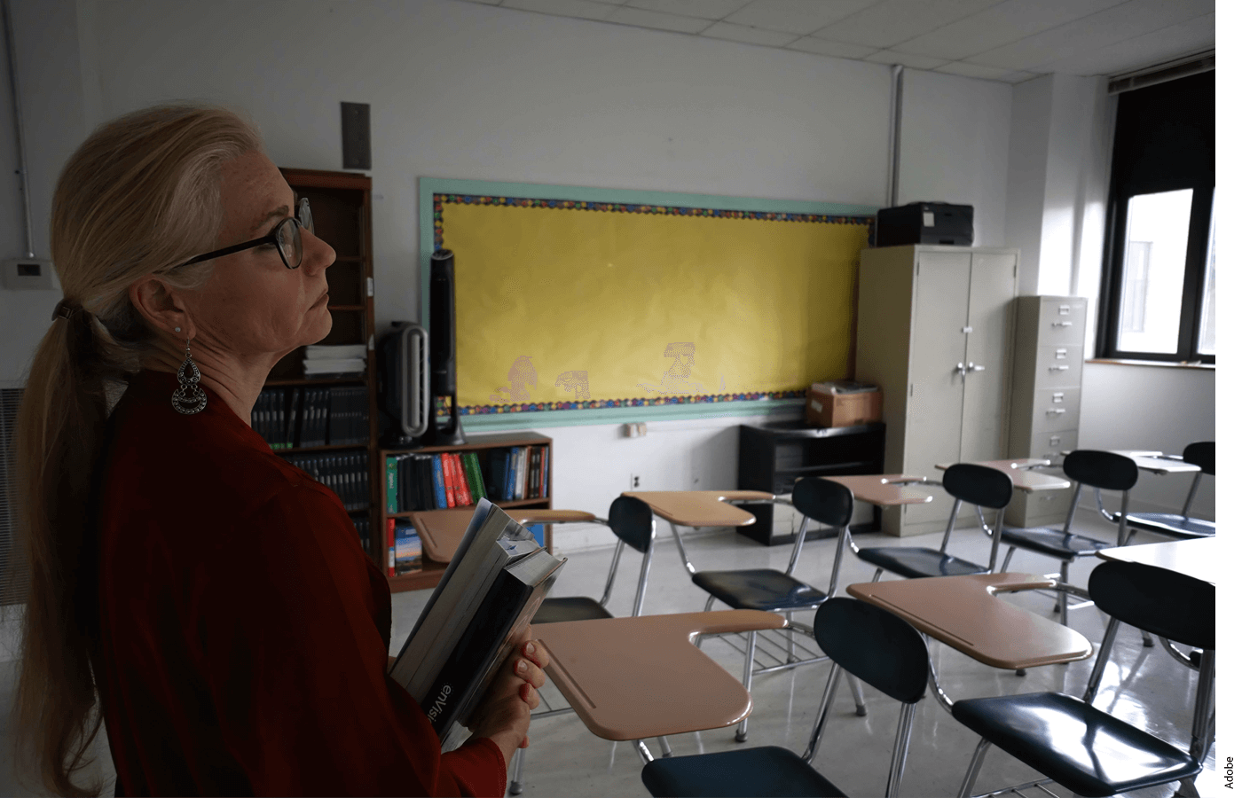 A teacher stands at the front of an empty classroom