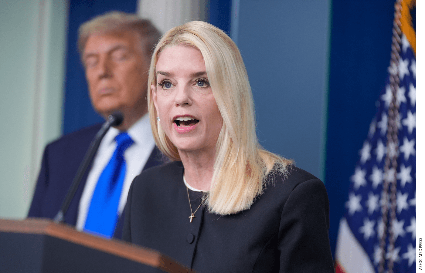 Attorney General Pam Bondi speaking at a podium with President Donald Trump behind her