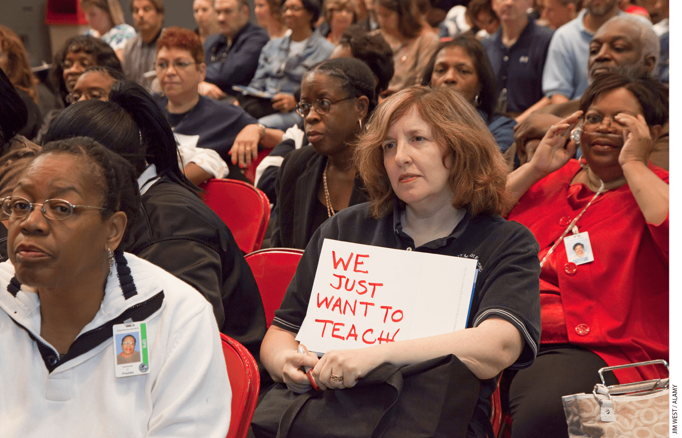 A teacher holds a "We just want to teach" sign at a union meeting