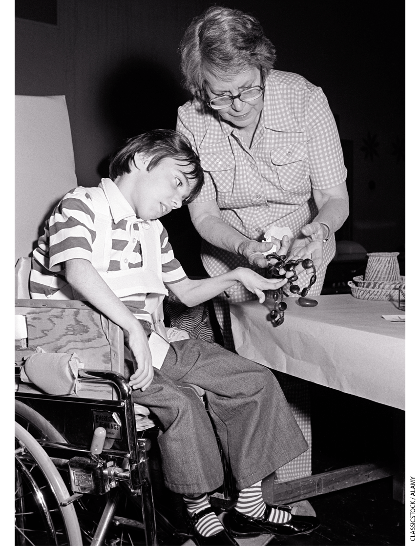 A student in a wheelchair works with an instructor at school in 1969.