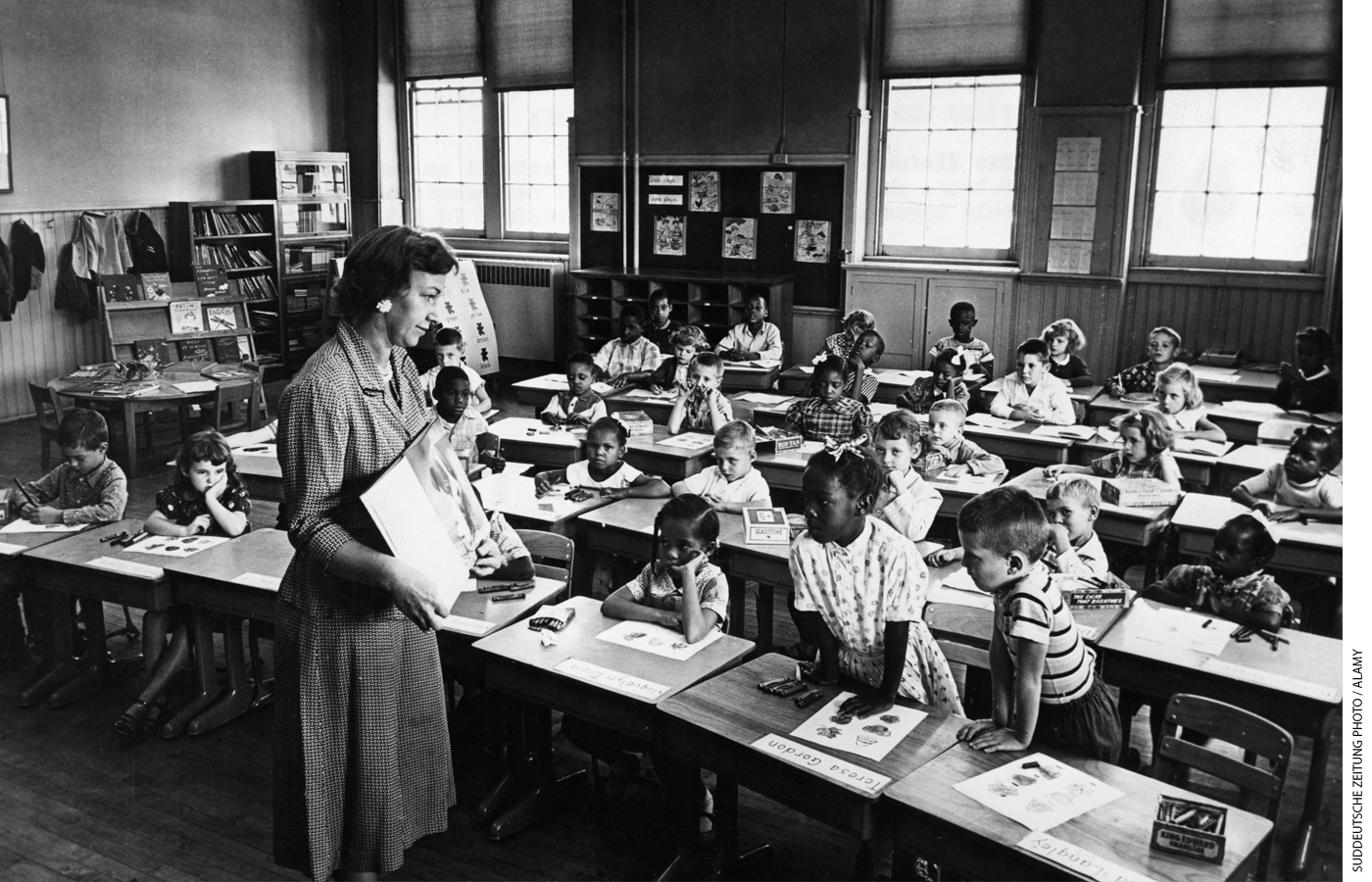 Photo of a teacher holding up a book in class as students look on