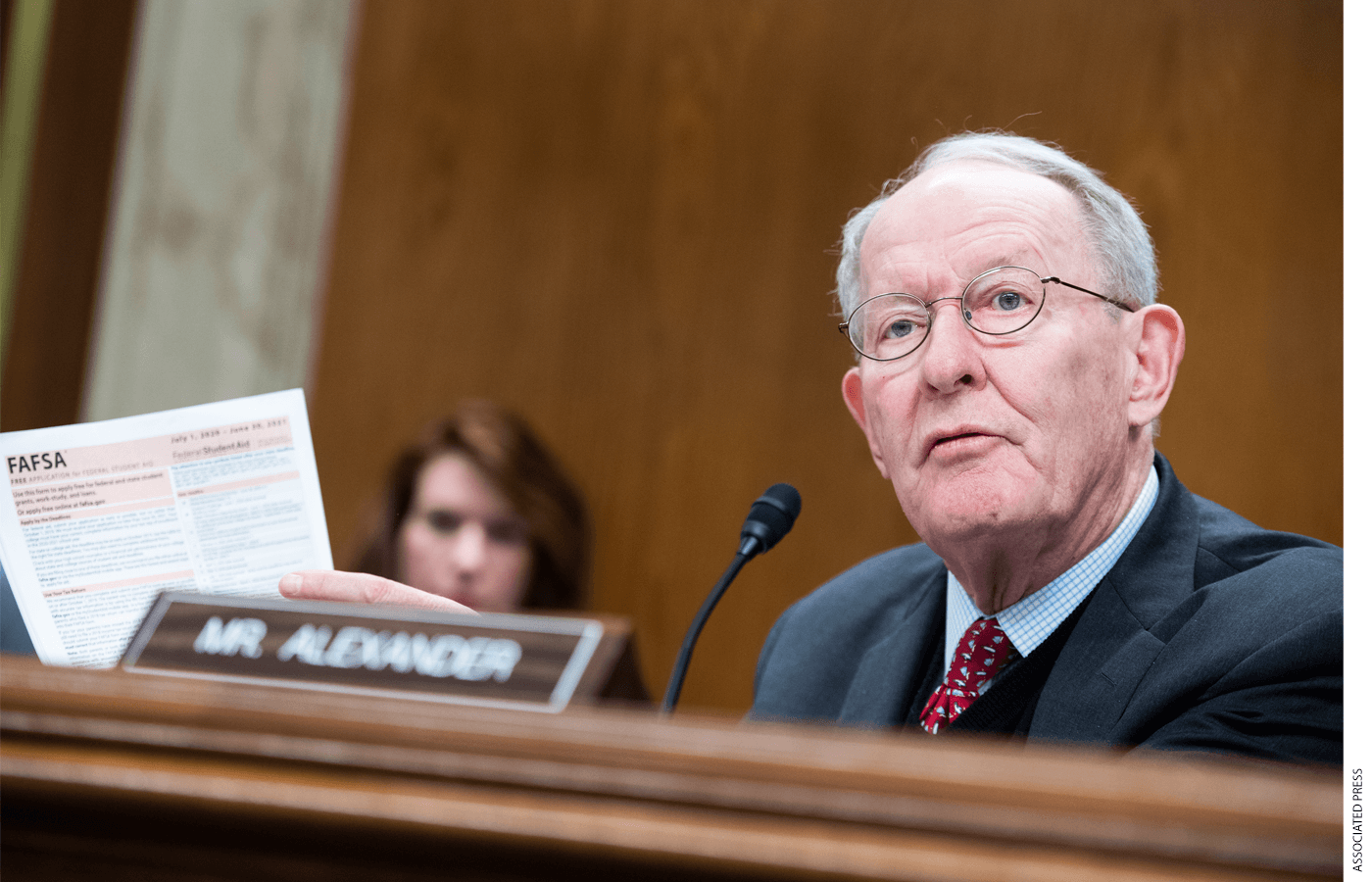 Photo of Senator Lamar Alexander seated while holding and pointing to a FAFSA form